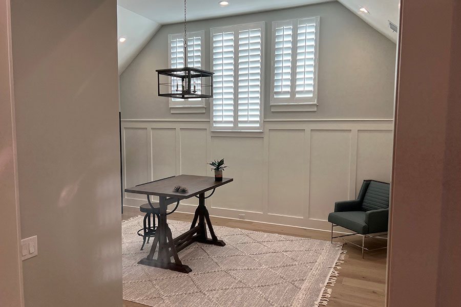 View through a doorway into a gray living space with white interior shutters on three windows