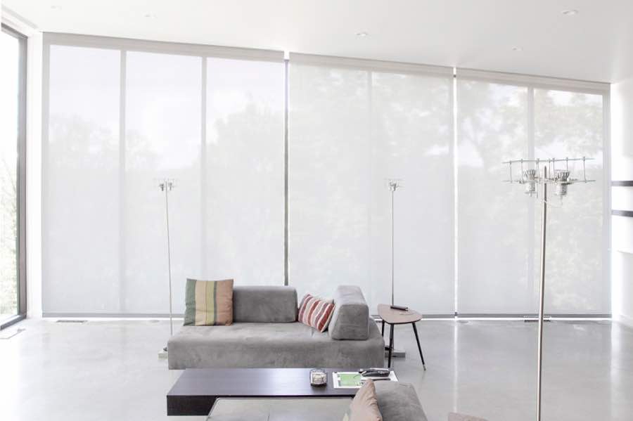 Motorized window shades make controlling natural light effortless in your Minneapolis great room. White motorized shades on a wall of tall great room windows